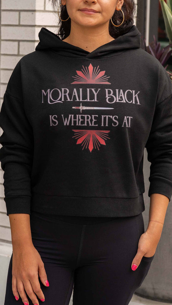 Girl wearing lightweight comfy hoodie with the phrase, "Morally Black is Where it's At" printed on the front with a dagger and bright red starbust details. The hoodie is slightly cropped length and black.