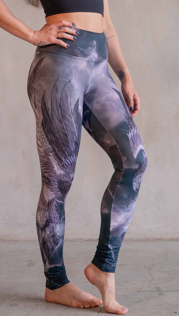 Model wearing WERKSHOP Thunderbird Athleisure Leggings. The artwork printed on the leggings features a thunderbird flying through a stormy sky with lightening. The leggings feature a closed colour pallete with all shades of purple.