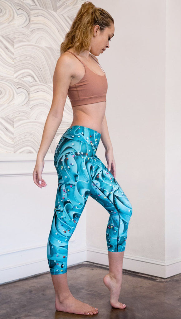 right side view of model wearing teal cupcake frosting themed printed capri leggings