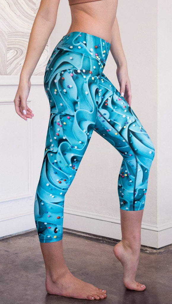 closeup right side view of model wearing teal cupcake frosting themed printed capri leggings