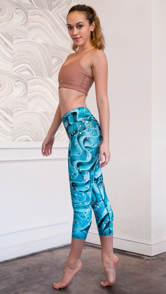 left side view of model wearing teal cupcake frosting themed printed capri leggings